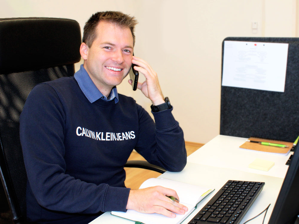 Portrait von Mitarbeiter Patrick Fally während er gerade am Computer sitzt und telefoniert.