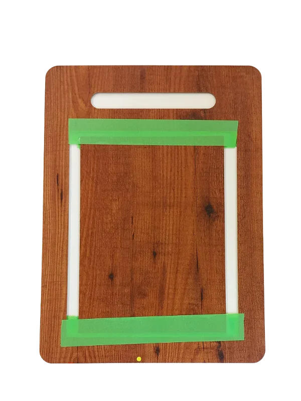 Wooden cutting board with green tape marking a rectangular cutout area, top handle visible.